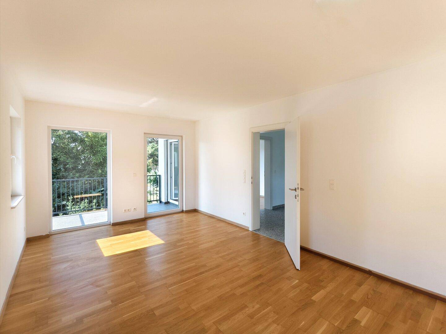 Geräumiges Schlafzimmer mit Holzboden und Zugang zum Balkon, der viel Licht hereinlässt.