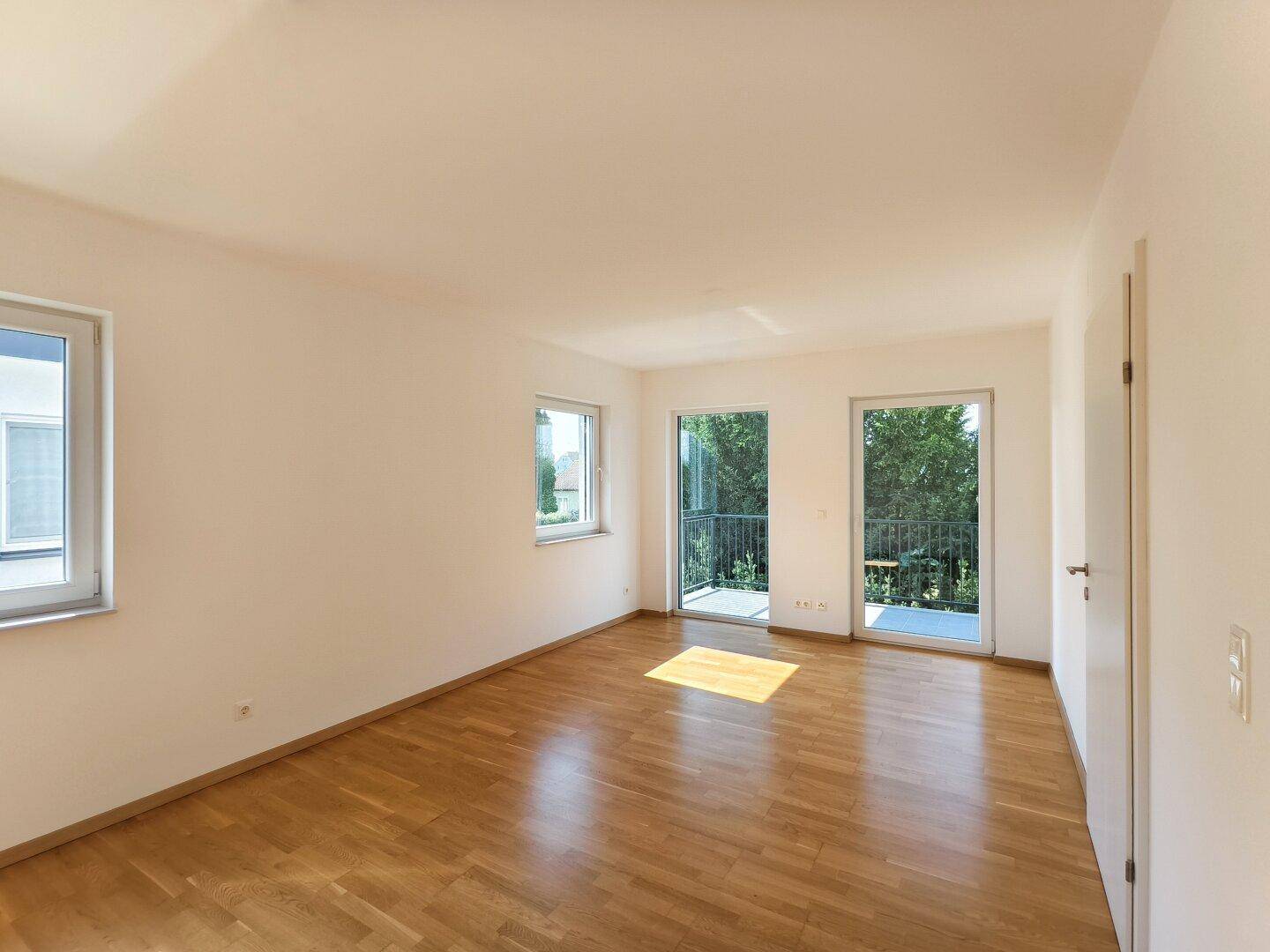 Helles Schlafzimmer mit Holzboden, großen Fenstern und direktem Zugang zum Balkon.