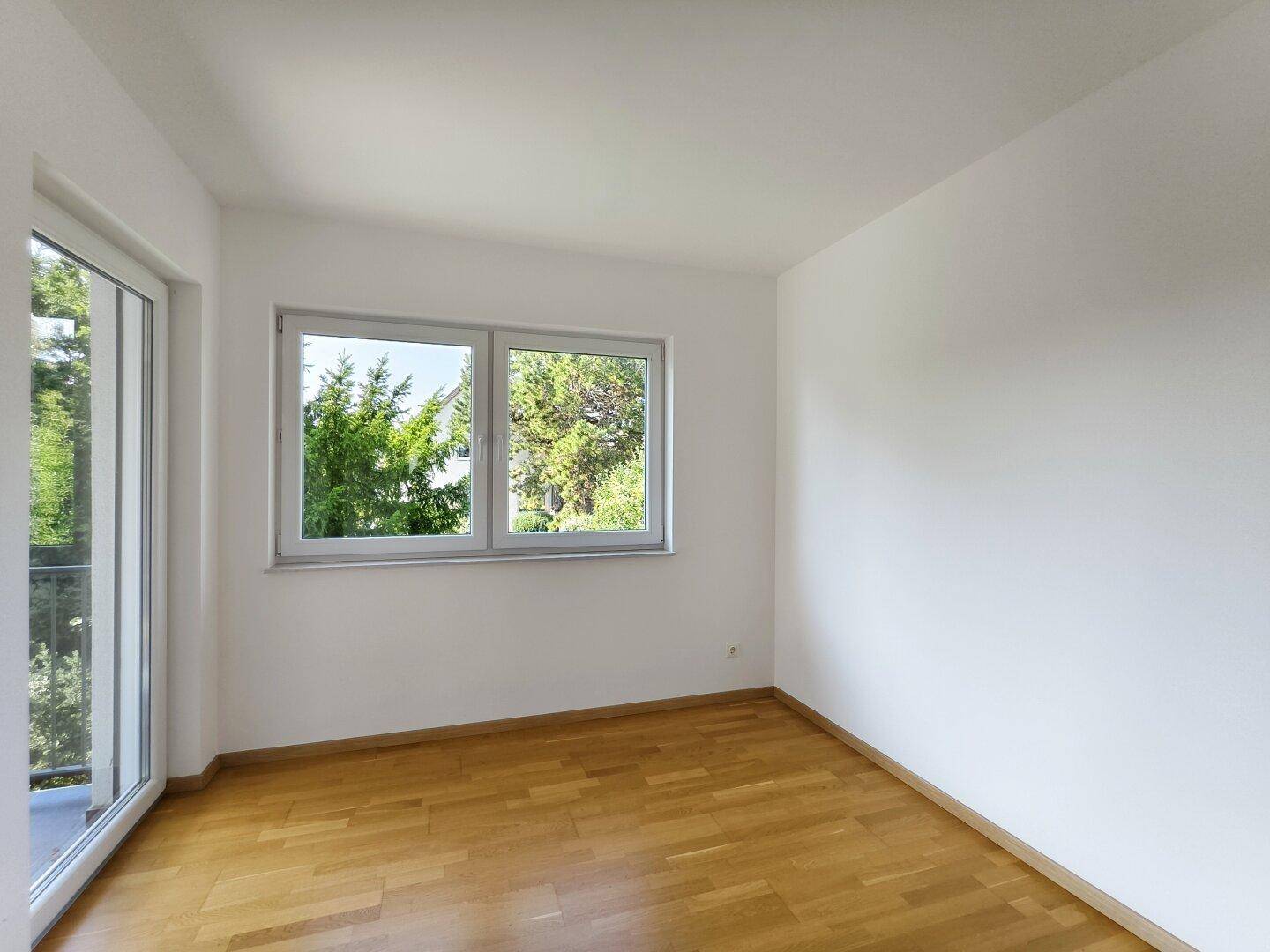 Schlafzimmer mit Holzboden und großen Fenstern, die einen schönen Blick ins Grüne bieten.