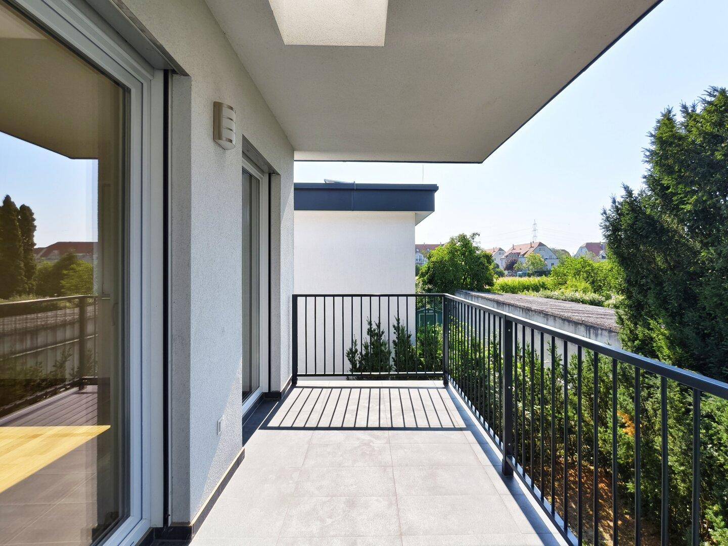 Heller Balkon mit Fliesenboden und schwarzem Geländer, bietet einen weiten Blick ins Grüne.