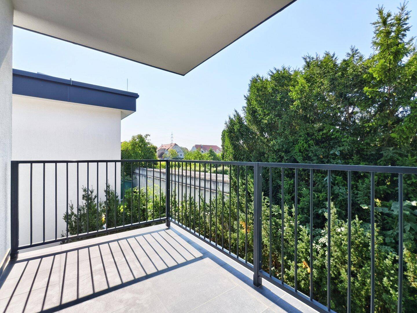 Sonniger Balkon mit Fliesenboden und Blick auf Bäume und die Umgebung.