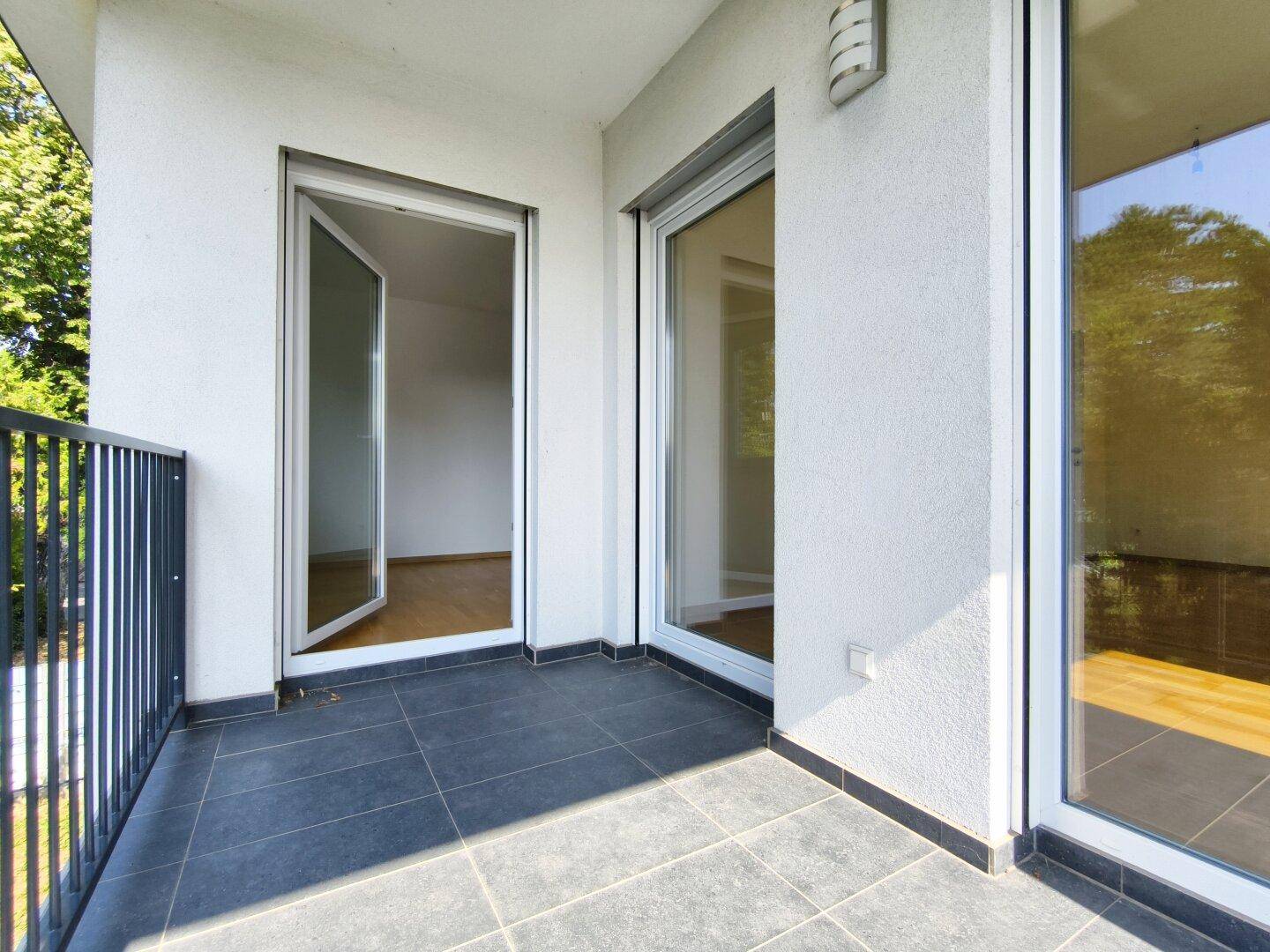 Balkon mit Fliesenboden und Zugang zu Innenräumen durch große Fenstertüren.