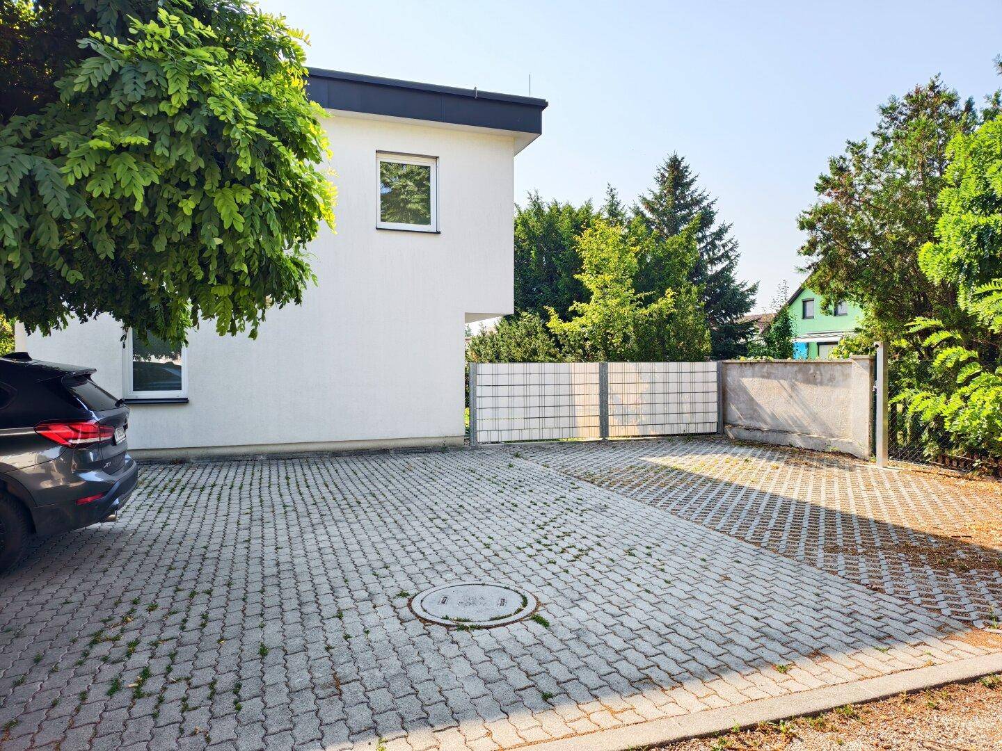 Gepflasterter Parkplatz neben dem modernen Gebäude mit viel Grün.