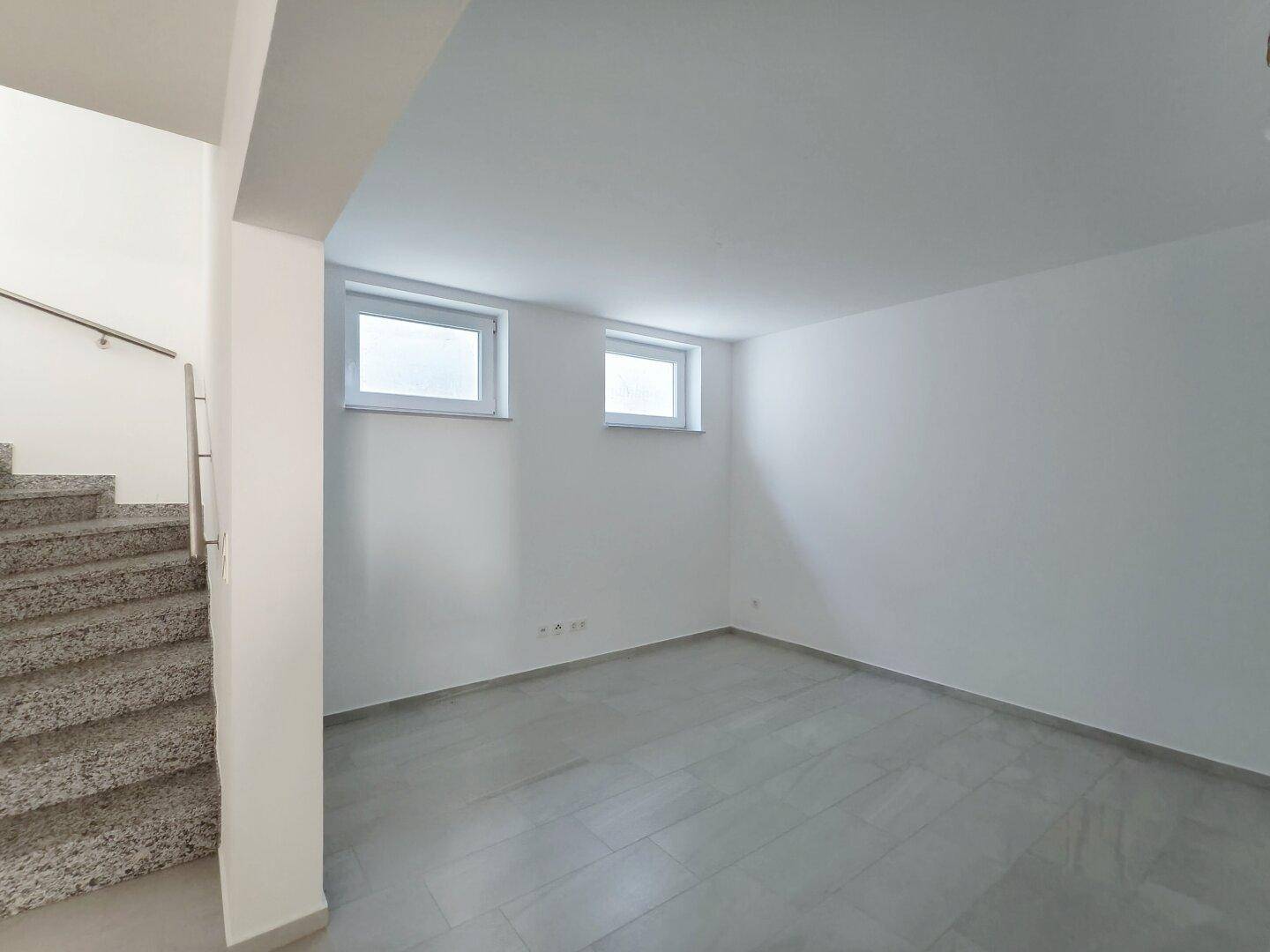 Geräumiger Kellerraum mit Fliesenboden und zwei kleinen Fenstern für Tageslicht.