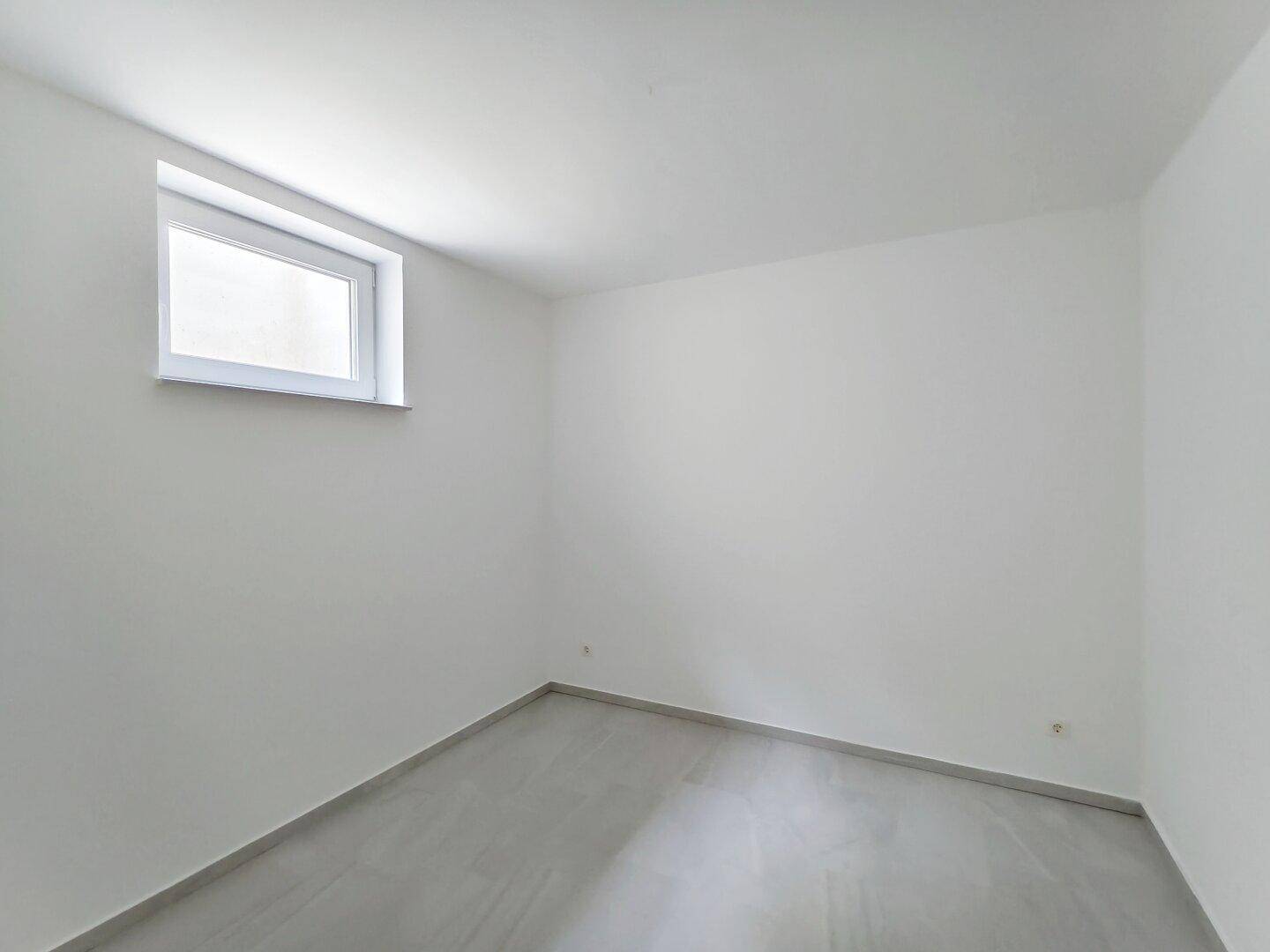 Helles Zimmer im Untergeschoss mit Fliesenboden und einem Fenster.