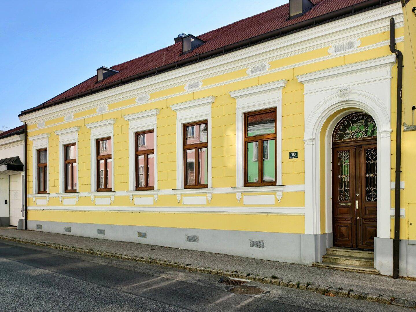 Historisches Gebäude mit gelber Fassade, Stuckelementen und großer Holztür an der Straße.