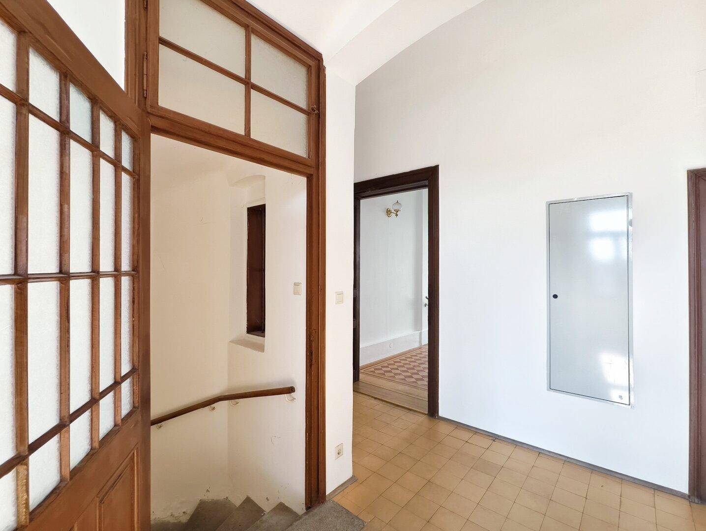 Heller Flur mit Holztreppe und gefliestem Boden, der zu weiteren Räumen führt.