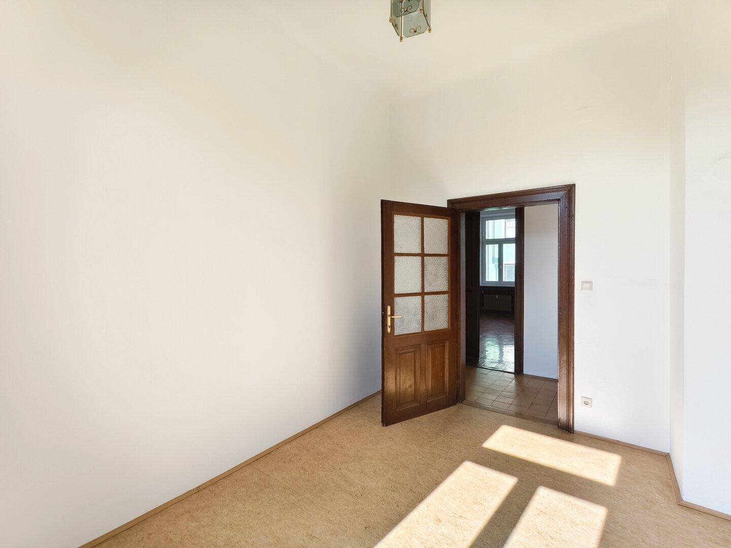 Gemütliches Zimmer mit Teppichboden und einer Holztür, die zu einem anderen Raum führt.