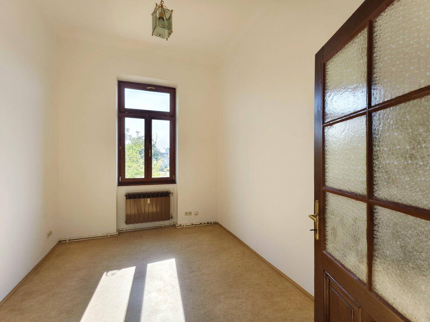 Helles Zimmer mit Teppichboden und einem Fenster, das viel Tageslicht hereinlässt.