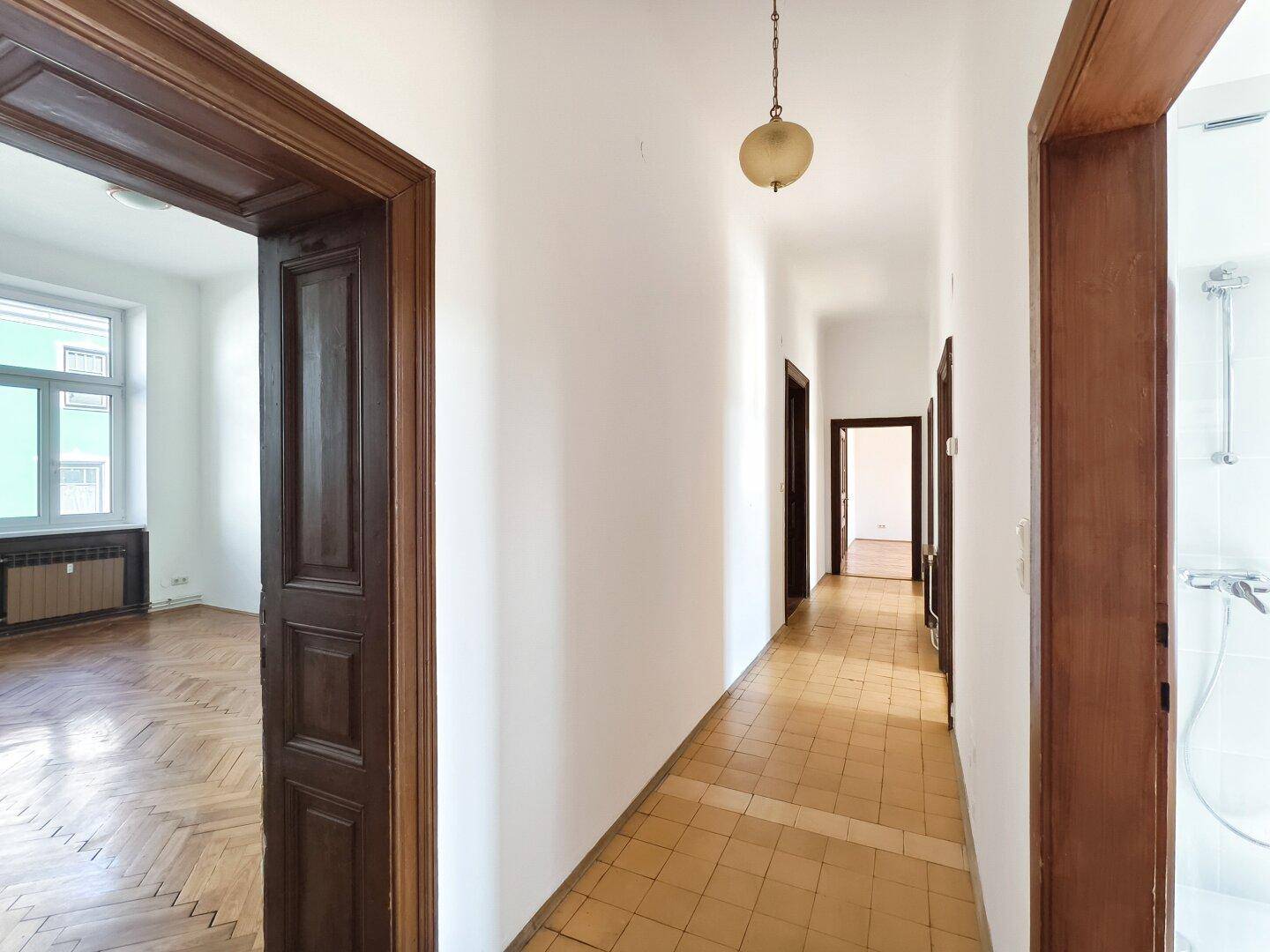 Heller Flur mit Fliesenboden und Blick in ein angrenzendes Zimmer mit Parkett.