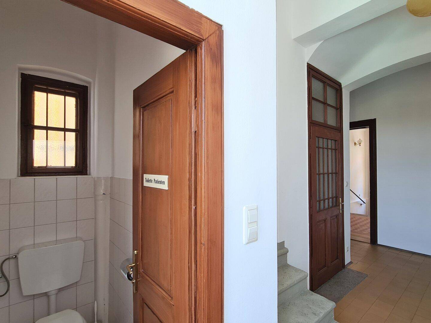 Einfache Gästetoilette mit Fenster, weißen Fliesen und Holzfensterrahmen.