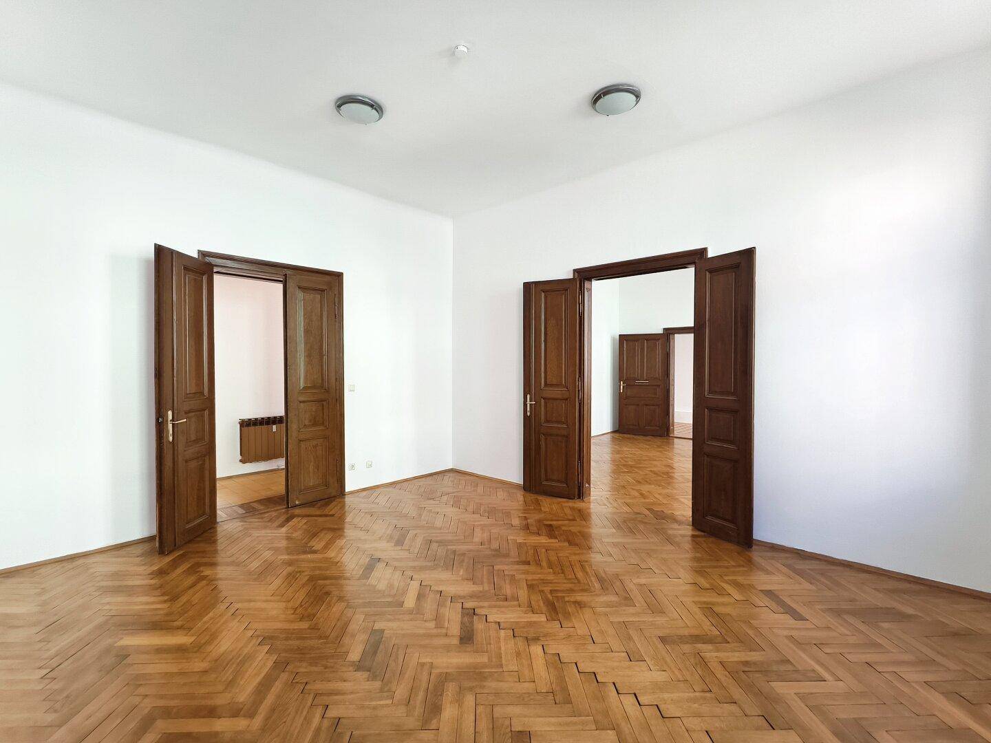 Großes Zimmer mit Fischgrätparkett und mehreren offenen Holztüren, die Räume verbinden.