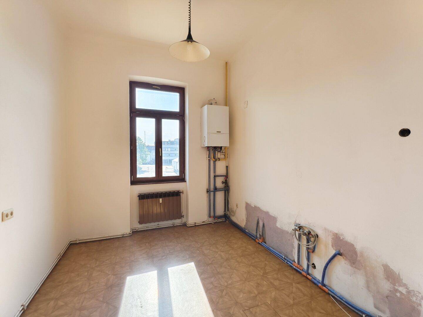 Leere Küche mit sichtbaren Anschlüssen für Geräte und einem Fenster.