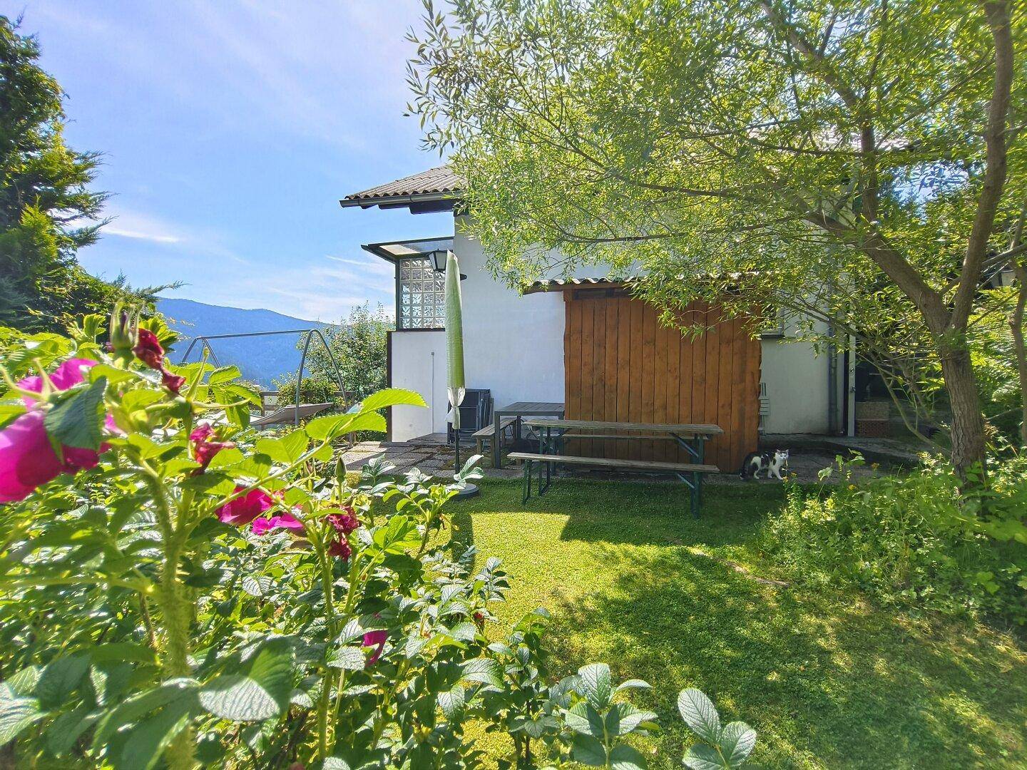 Idyllischer Gartenbereich neben dem Haus mit Picknicktisch, Blumen und Bergblick.