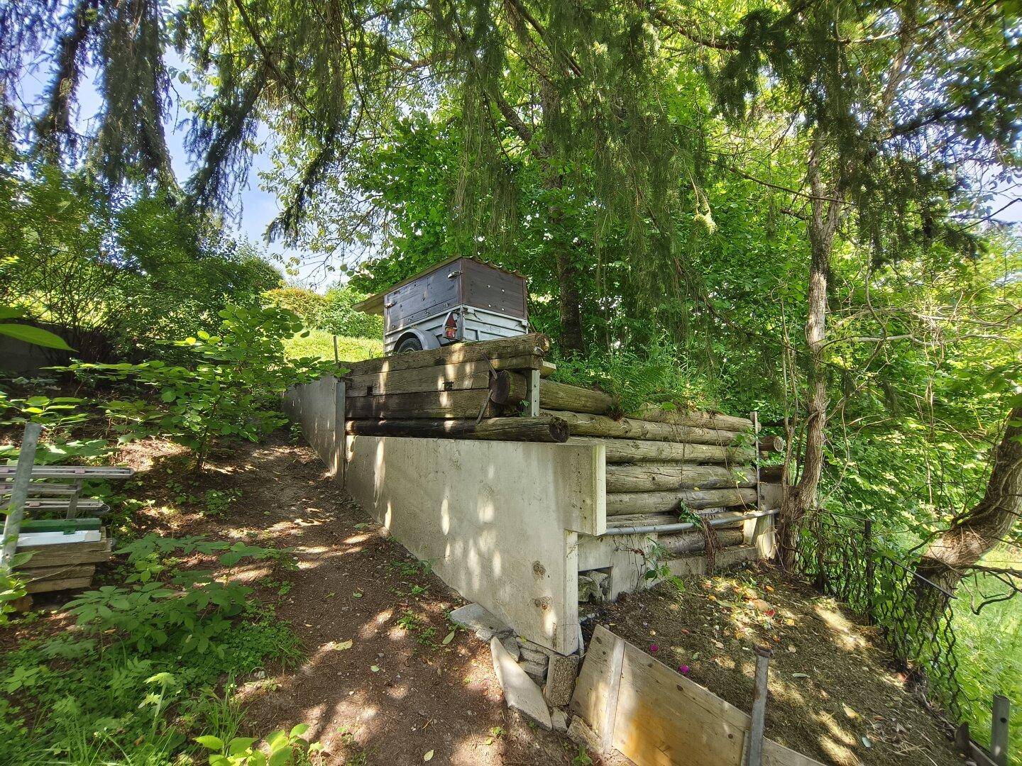 Rustikales Lagergebäude aus Holzstämmen, in den Hang gebaut, umgeben von Bäumen.