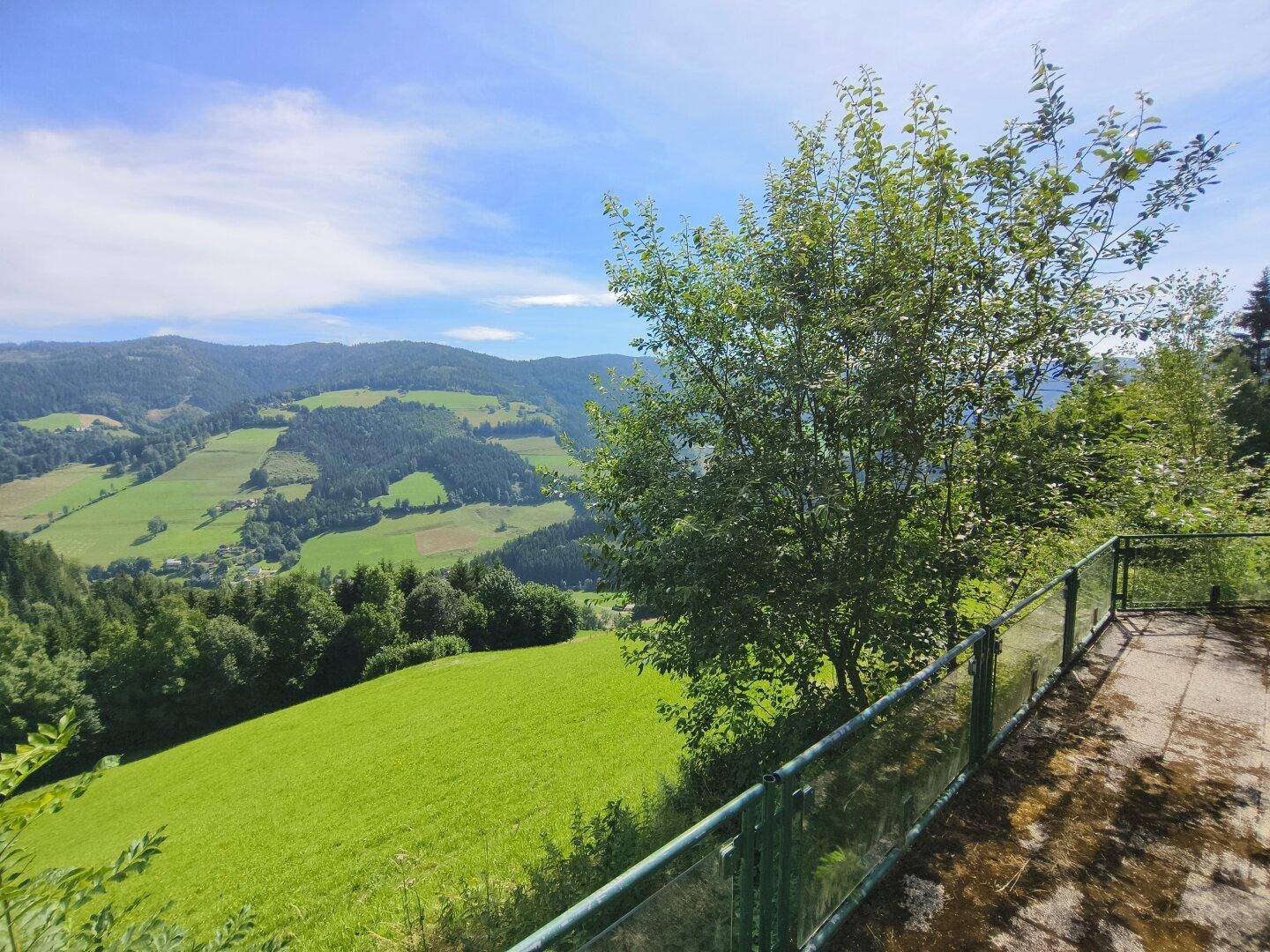 Große gepflasterte Terrasse mit Geländer und weitem Panoramablick auf die grüne Berglandschaft.
