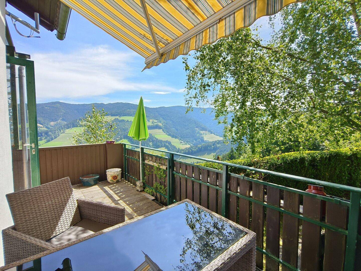 Gemütlicher Balkon mit Markise, Sitzgelegenheiten und weitem Blick über die grüne Landschaft.