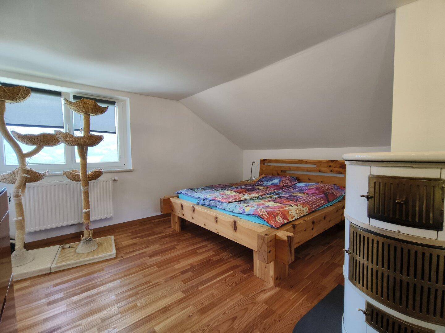 Schlafzimmer im Dachgeschoss mit Holzbett, Kachelofen und schrägen Wänden.