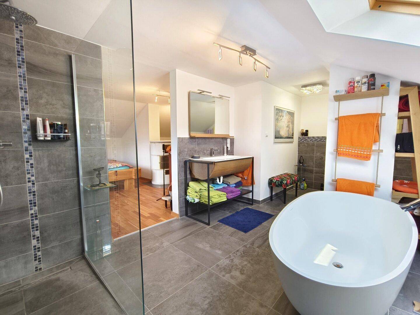 Großzügiges Badezimmer mit freistehender Badewanne, Dusche und Zugang zum Schlafbereich.