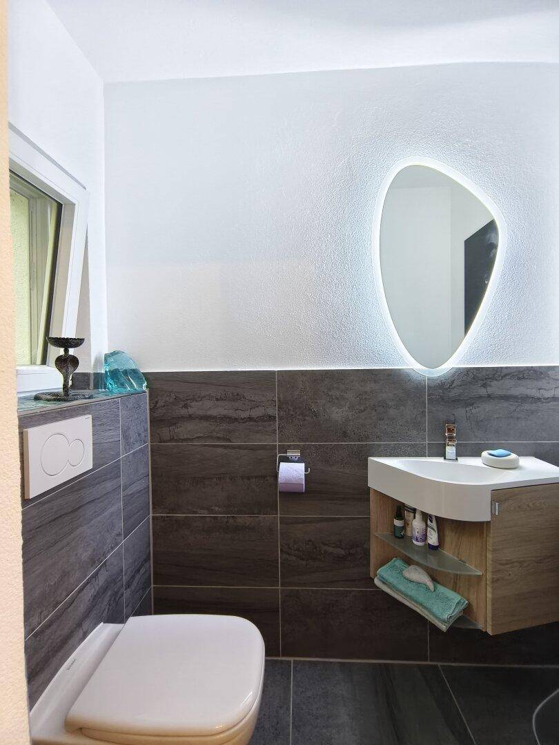 Modernes Gäste-WC mit beleuchtetem Spiegel, Wand-WC und stilvollem Waschtisch.