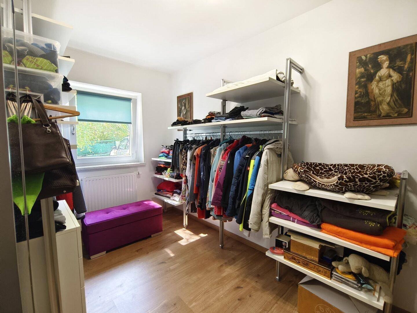 Geräumiger begehbarer Kleiderschrank mit viel Stauraum und Fenster für Tageslicht.