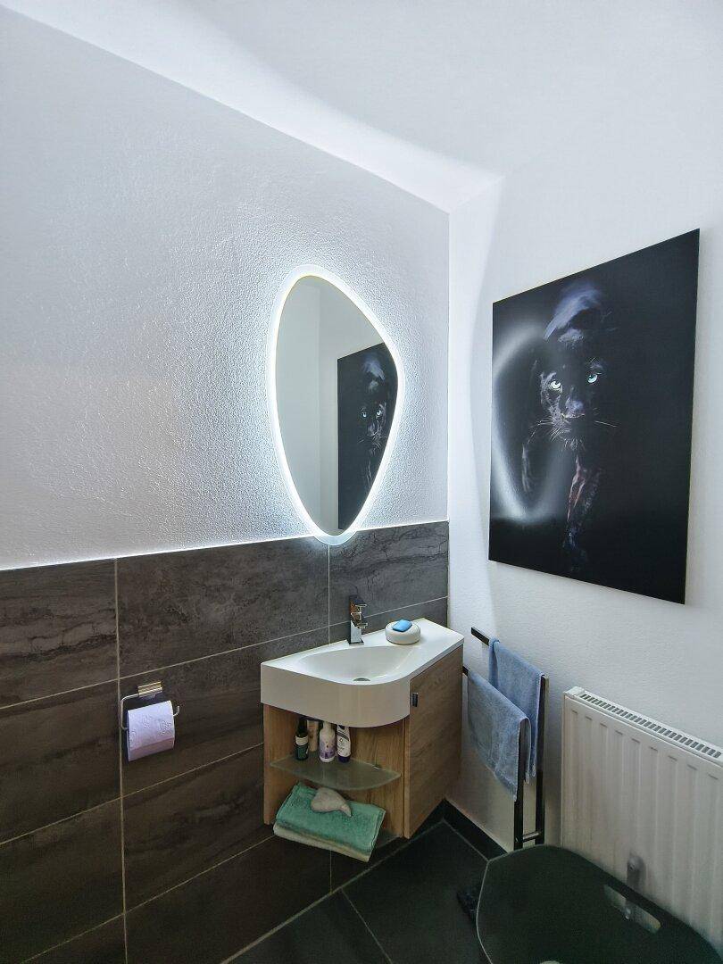 Stilvolles Gäste-WC mit beleuchtetem Spiegel, modernem Waschtisch und Heizkörper.