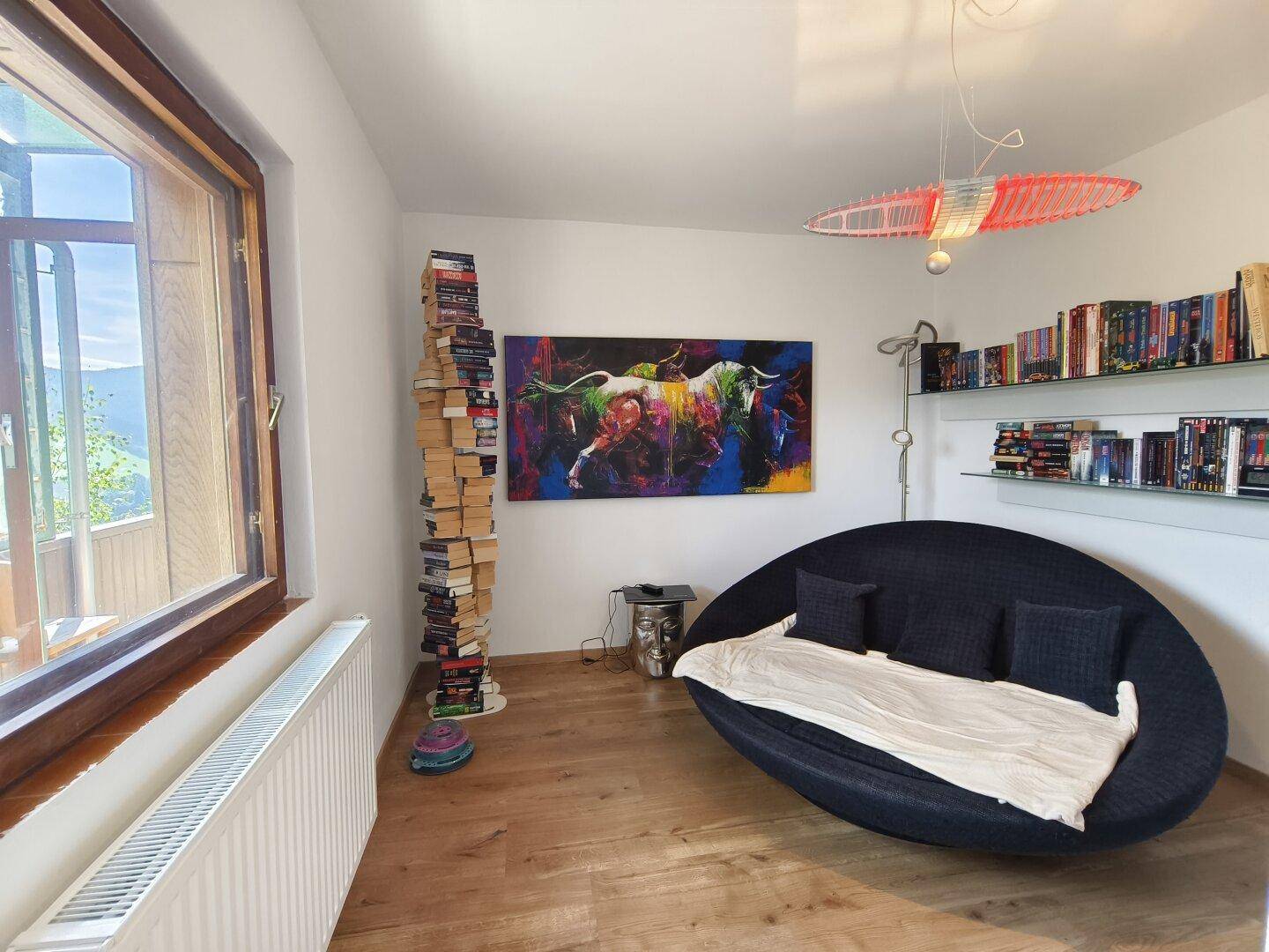 Gemütliches Wohnzimmer mit Holzboden, Kunst an der Wand und Blick ins Grüne.