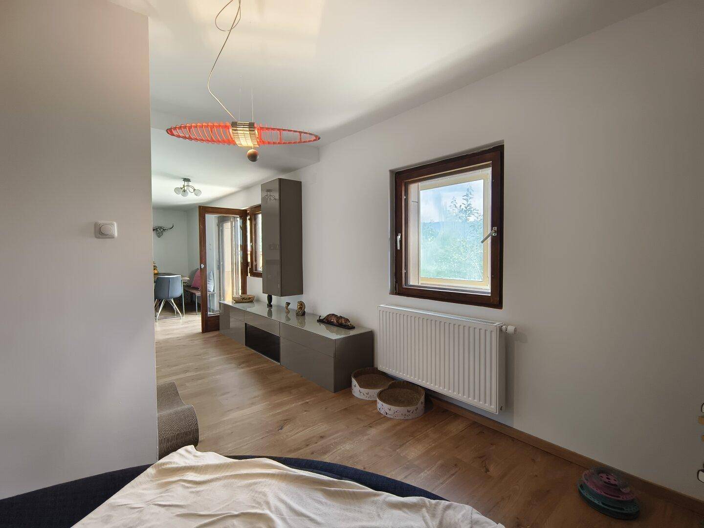 Helles Wohnzimmer mit Holzboden, Fenster und Blick in den Essbereich.