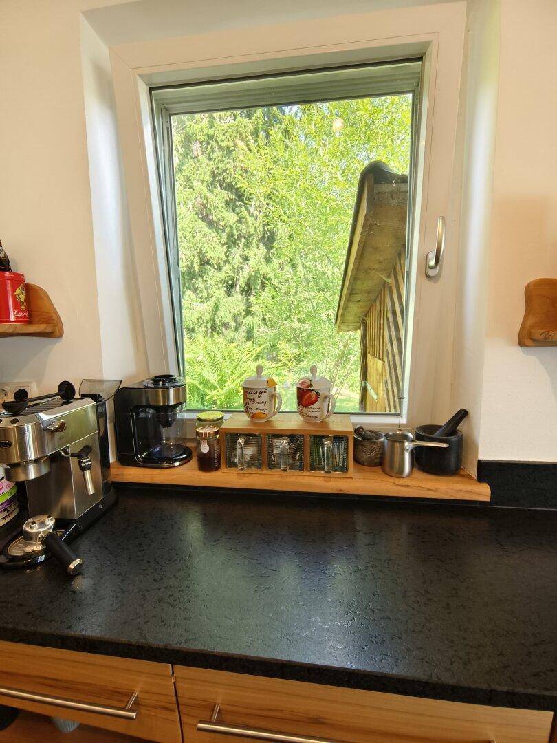 Küchenzeile mit schwarzer Arbeitsplatte, Kaffeemaschine und Blick ins Grüne durch das Fenster.