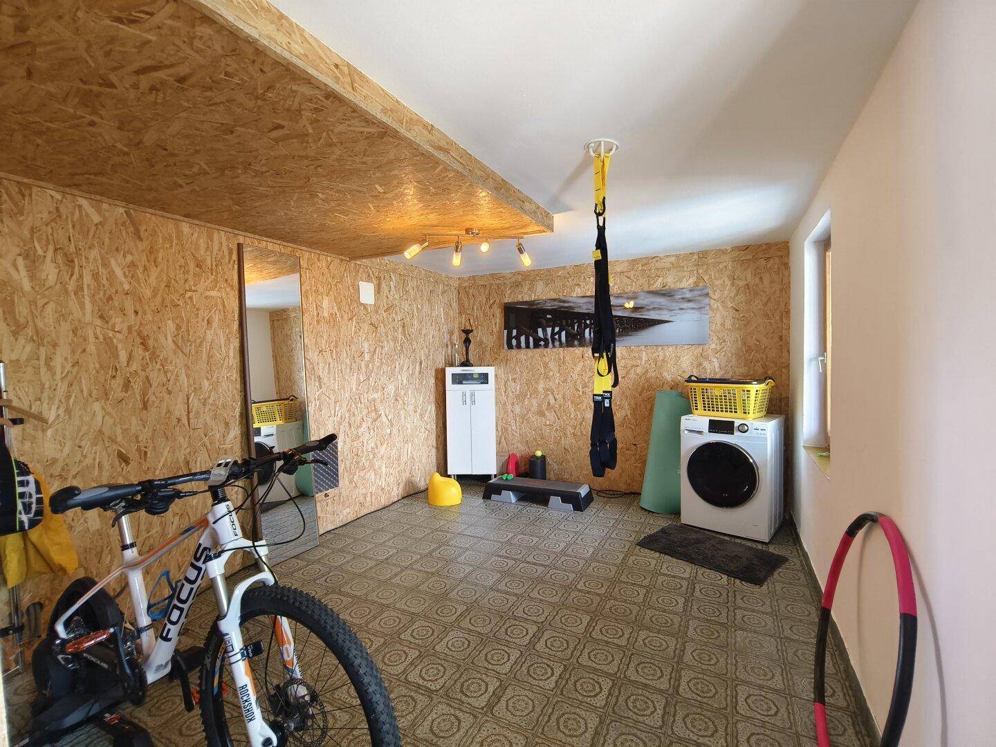Vielseitiger Raum mit OSB-Platten, Waschmaschine und Fitnessgeräten.