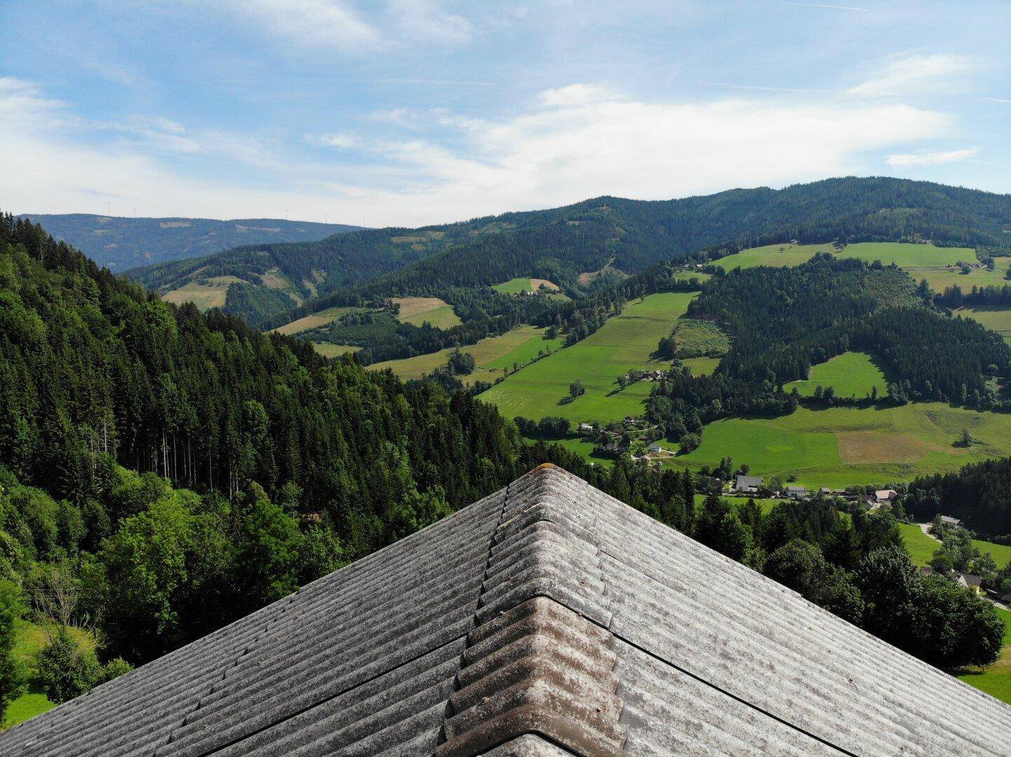 Blick über das Dach des Hauses auf die grünen Hügel und das weite Tal.