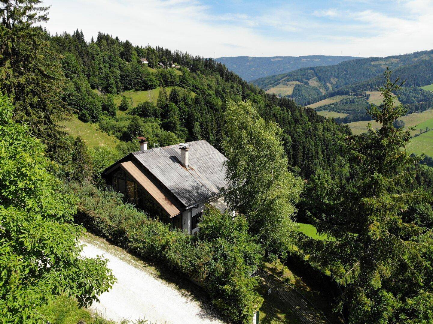 Luftaufnahme des Hauses von oben, mit Blick auf das Dach und den umliegenden Wald.