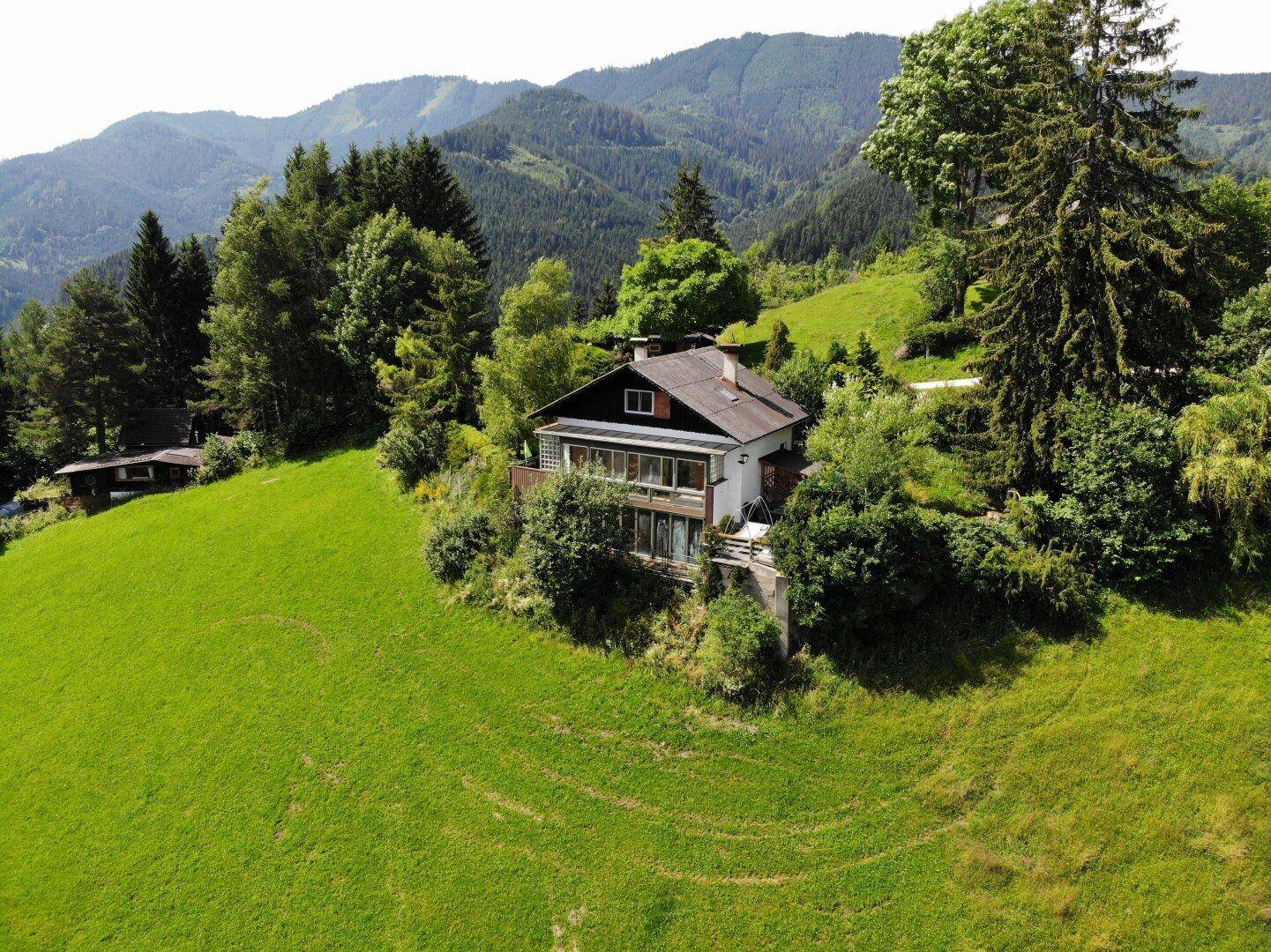 Weitläufige Luftaufnahme des Hauses, eingebettet in die grüne Naturlandschaft mit sanften Hügeln.