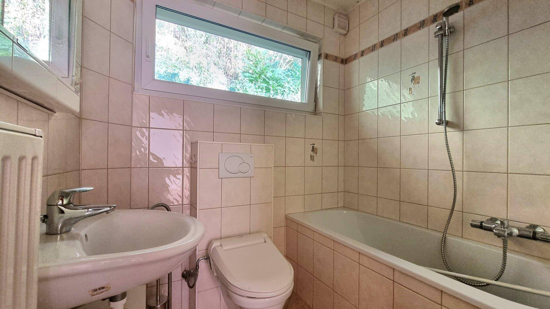 Badezimmer mit Badewanne, WC, Waschbecken und beigefarbenen Fliesen.