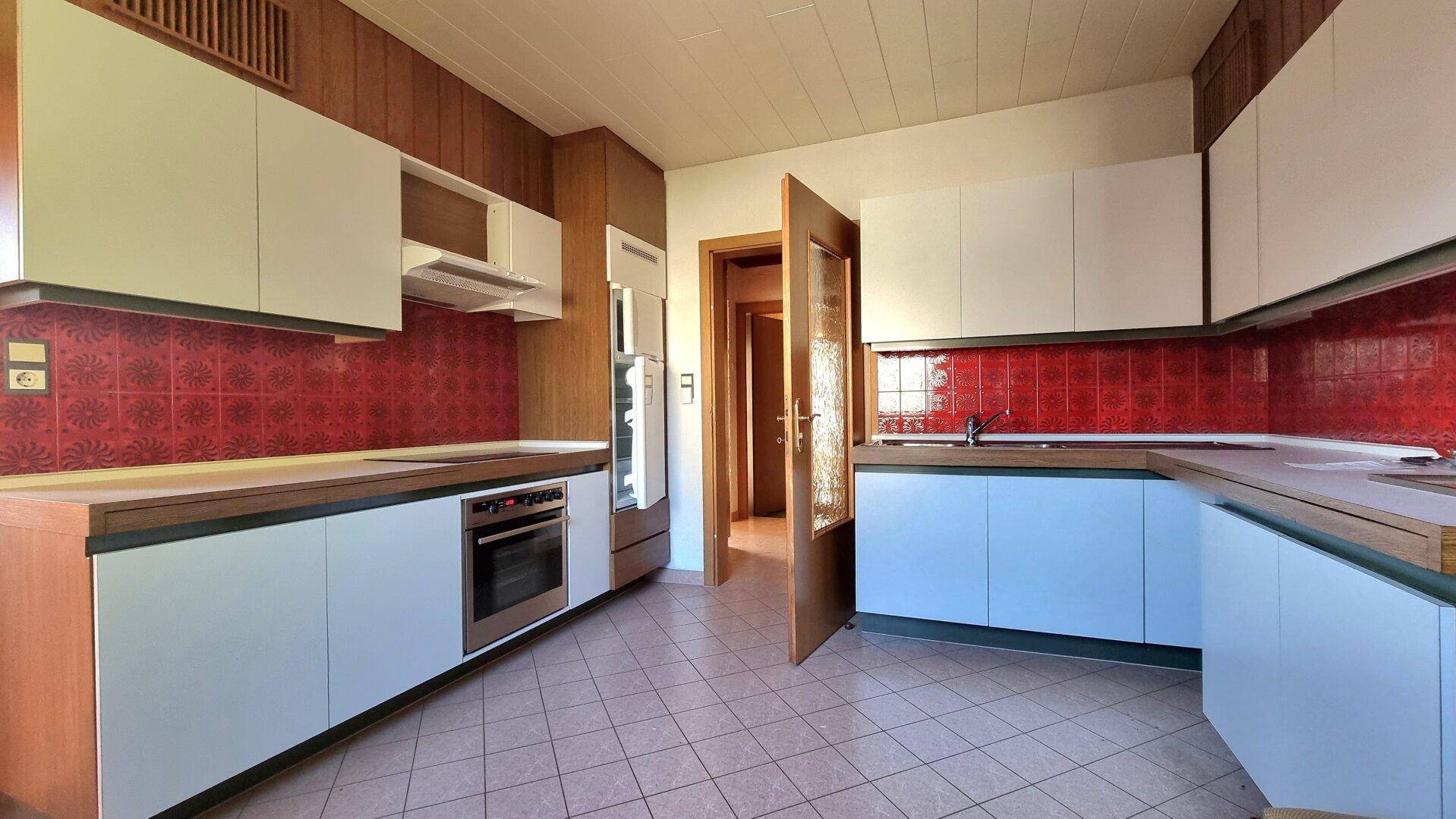 Küche mit roten Fliesen als Spritzschutz, Holzdetails und weißen Unterschränken.