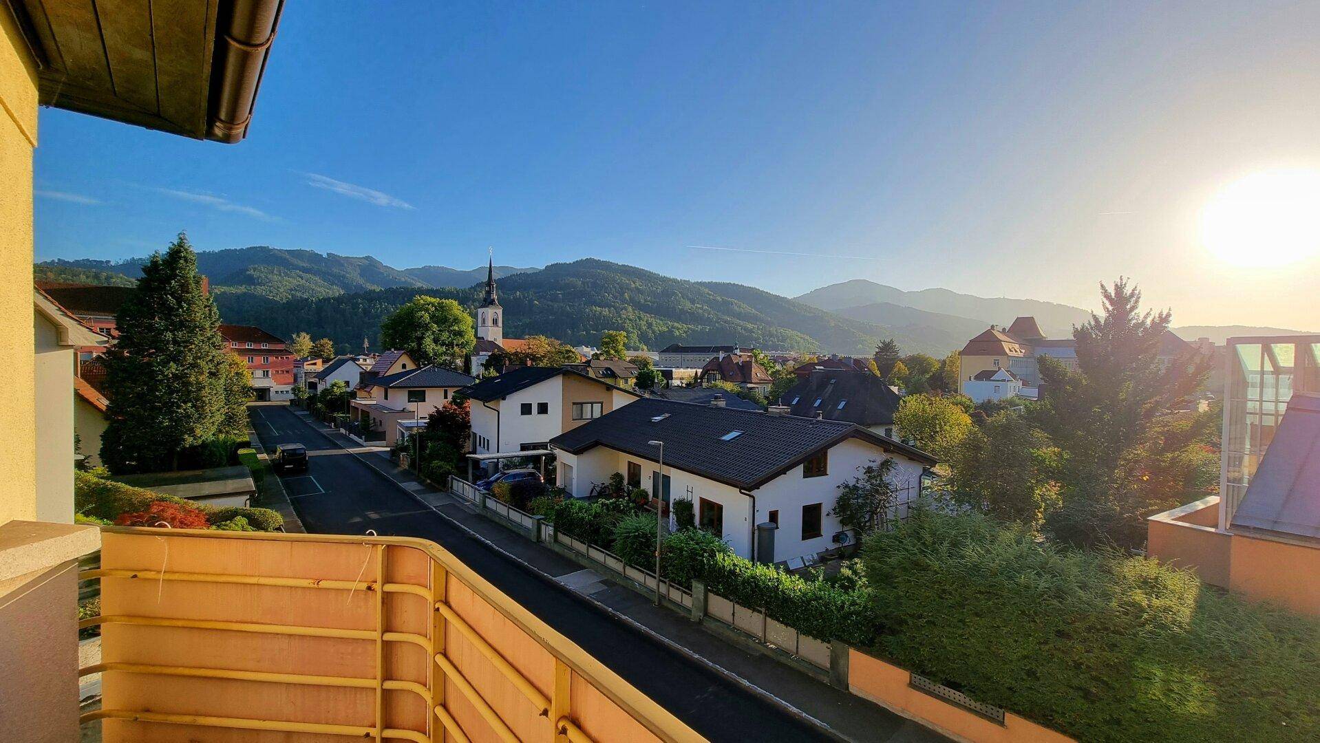 Panoramablick vom Balkon auf eine Stadt mit Bergen im Hintergrund bei Sonnenuntergang.