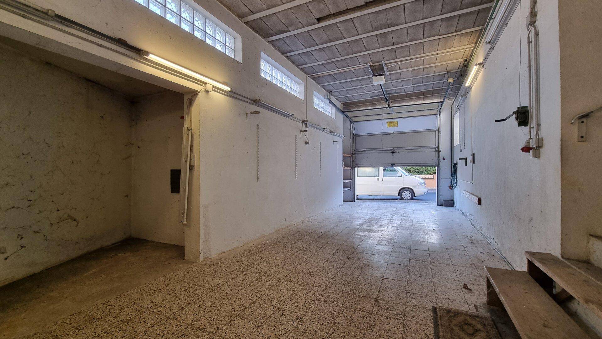 Geräumige Garage mit Fliesenboden und einem Rolltor, das nach außen führt.