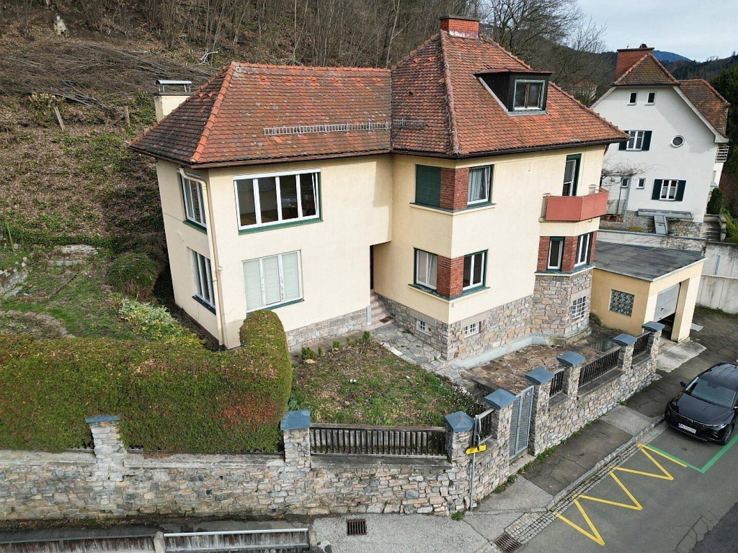 Luftaufnahme des gelben Hauses mit Garten, Garage und angrenzender Straße.