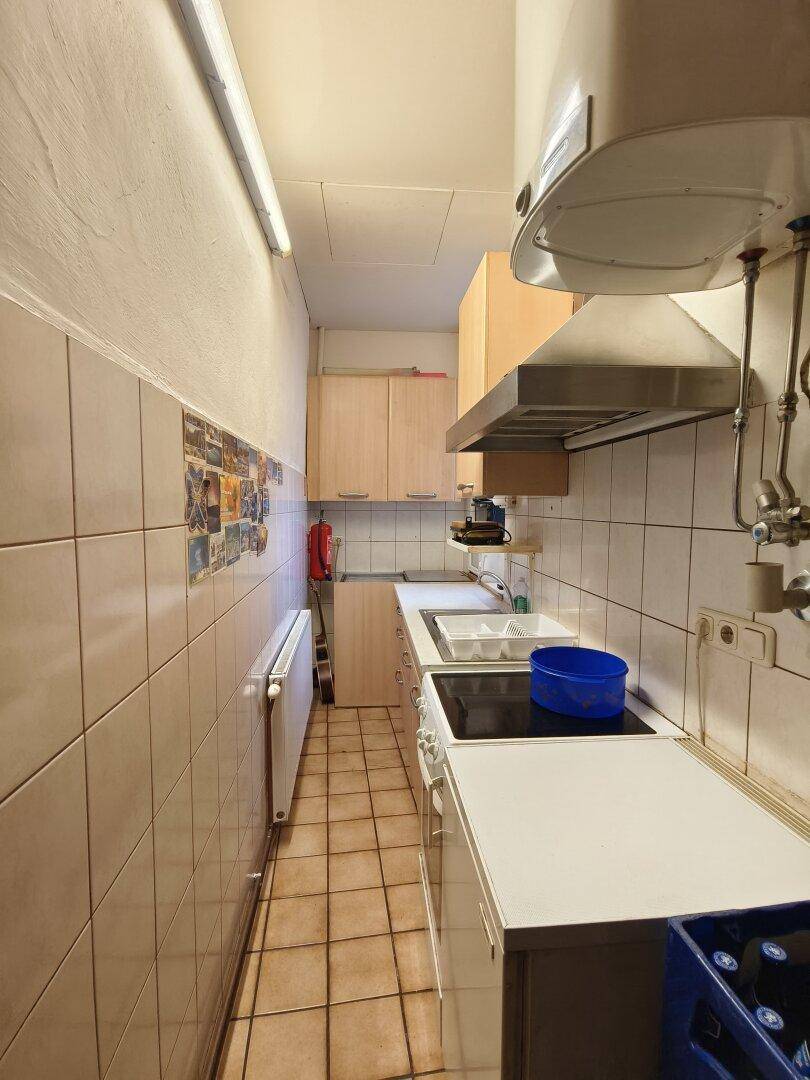 Schmale Küche mit weißen Fliesen, einfacher Ausstattung und einem Warmwasserboiler an der Wand.