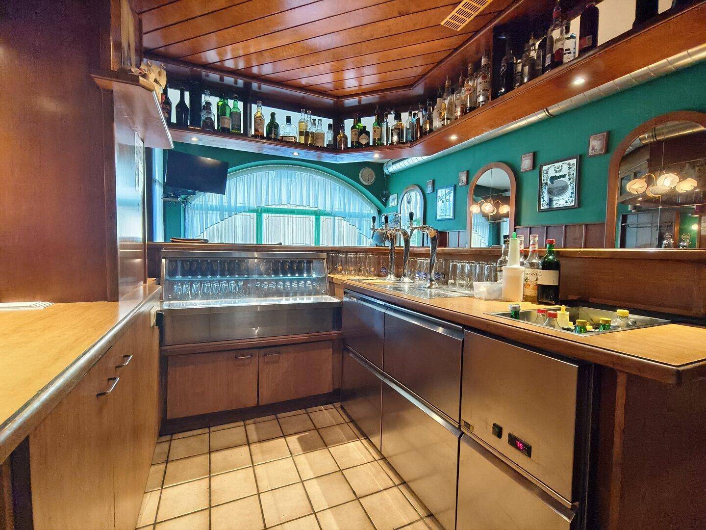 Nahaufnahme des Barbereichs mit Edelstahlgeräten, Zapfanlage und gefüllten Gläserregalen.