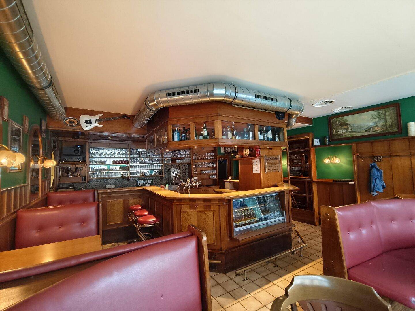 Weitläufiger Barbereich mit Holzelementen, roten Sitzbänken und einer Gitarre als Dekoration an der Wand.