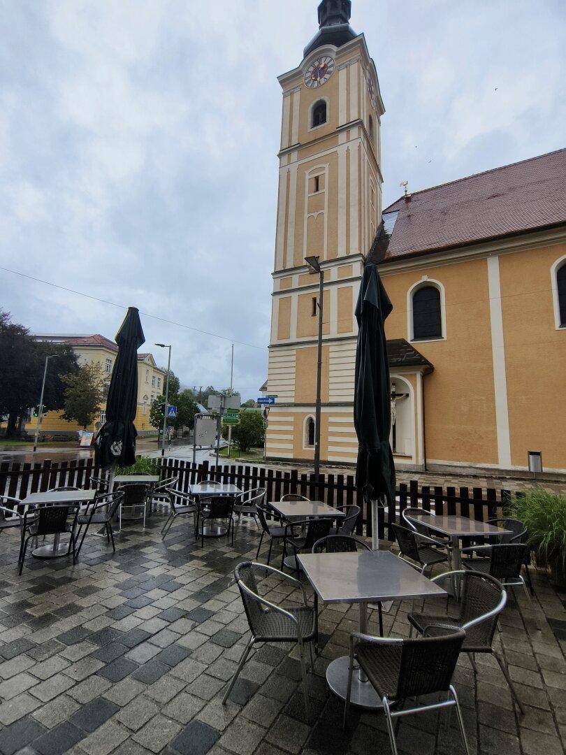 Außenterrasse mit Tischen und Stühlen vor einer historischen Kirche unter bewölktem Himmel.