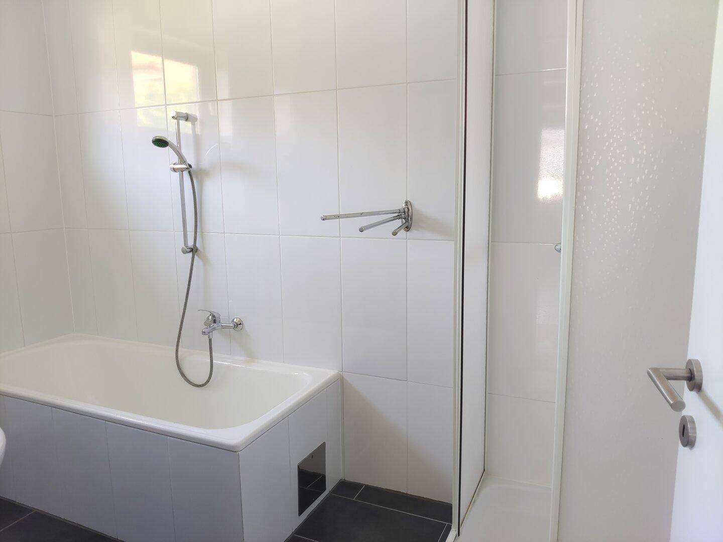 Modern gefliestes Badezimmer mit Badewanne, Duschbereich und weißen Wandfliesen.