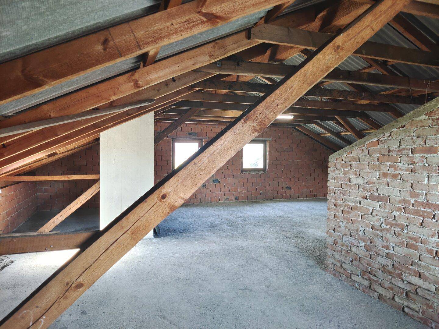 Geräumiger Dachboden mit sichtbaren Holzbalken und Ziegelwänden, bereit zum Ausbau.