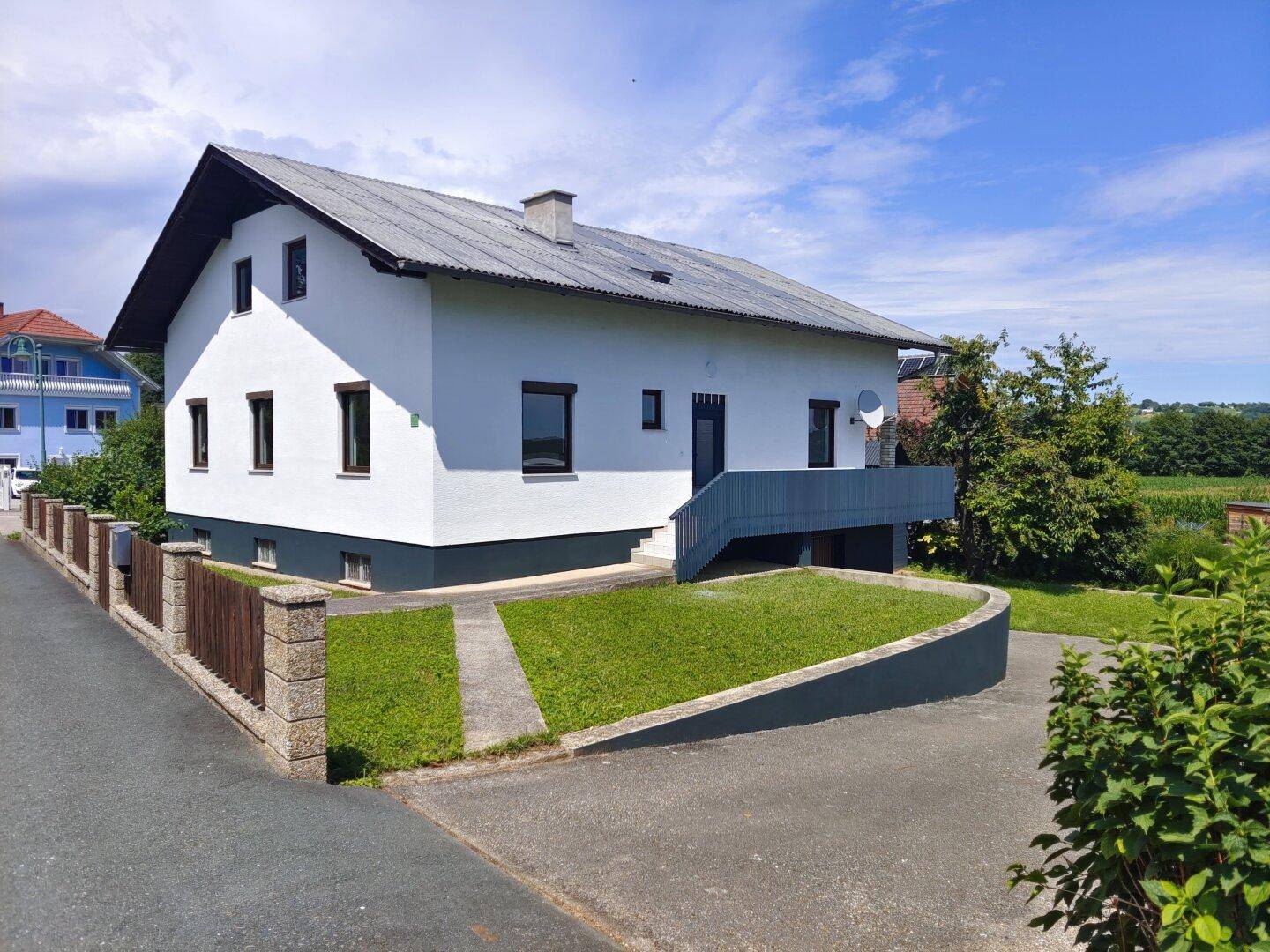 Vorderseite des Hauses mit weißer Fassade, dunklem Sockel und gepflegtem Vorgarten.