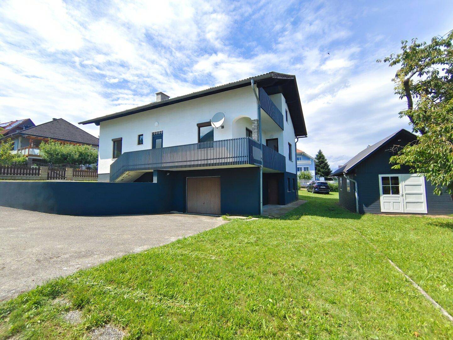 Seitenansicht des Hauses mit Garagenzufahrt, Gartenhaus und großem Rasenbereich.