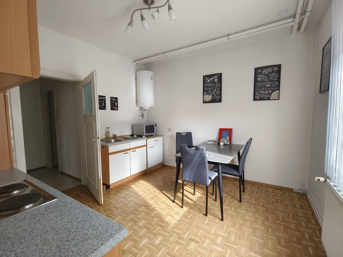 Küche mit Essbereich, einfachen weißen Schränken und Parkettboden.