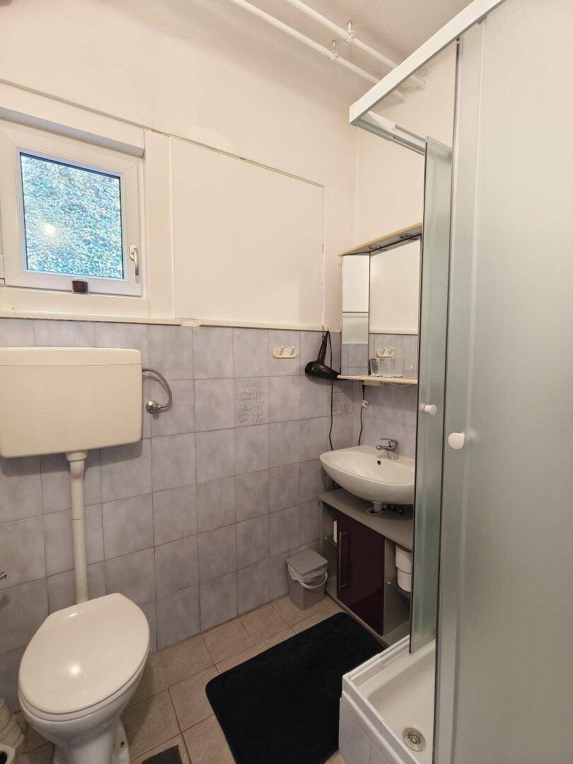 Kleines Badezimmer mit Dusche, WC, Waschbecken und einem Fenster.