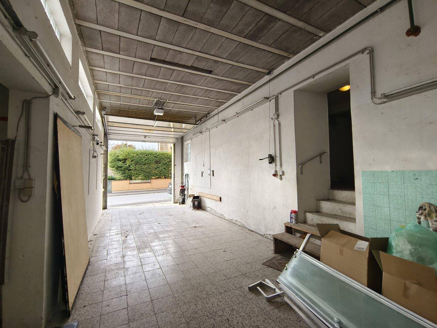 Geräumige Garage mit Fliesenboden und einem Rolltor, das nach außen führt.