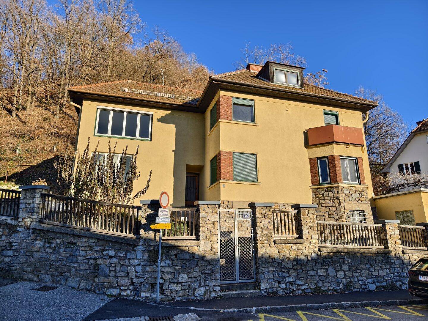 Gelbes Haus mit Ziegeldach und dekorativer Steinmauer entlang der Grundstücksgrenze.